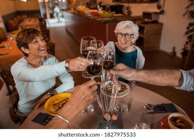 Senior Friends Group Celebrating At Dinner At Restaurant. Detail Of Hands While Toasting With Glasses Of Red Wine. Elderly Lifestyle, Friendship, Food And Drink, Retired And Pensioners Concept