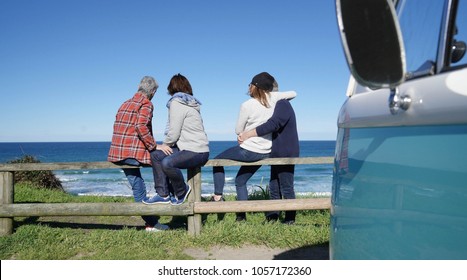 Senior friends on a road trip looking at the ocean, sit on fence - Powered by Shutterstock