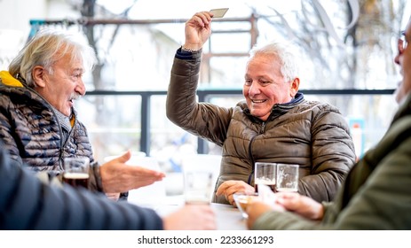 Senior friends playing cards at local bar on winter day - Ageless life style concept with mature people having fun together - Bright contrast filter - Powered by Shutterstock