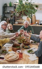 Senior Friends Sitting At The Table And Raising Glasses Of Red Wine During Dinner At Home