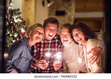 Senior Friends With Sparklers Next To Christmas Tree Having Fun.