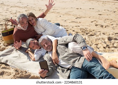 Senior friends taking selfie at beach on sunny day. Two middle-aged couples relaxing at sandy shore while gray-haired man holding smartphone and taking photo. Leisure, modern technology concept - Powered by Shutterstock