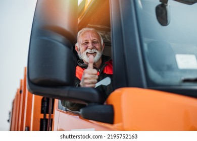 Senior garbage removal worker driving a waste truck. He is showing thumb up.
