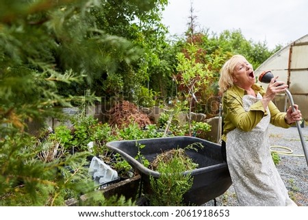 Senior gardener sings for hilarity in a garden hose in the nursery