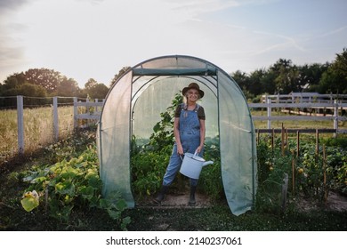 Senior gardener woman holding watering can in greenhouse at garden, looking at camera. - Powered by Shutterstock