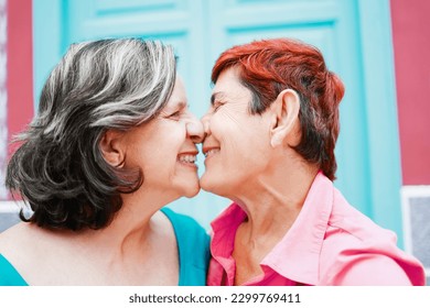 Senior gay lesbian couple kissing outside - LGBTQ aged tourists having tender moment during summer vacation