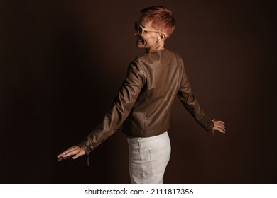 Senior Ginger Woman In Sunglasses Smiling While Dancing On Camera Isolated Over Brown Wall