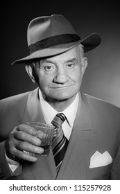 Senior Glamour Vintage Man Wearing Suit And Tie And Hat. Black And White Studio Shot. Gangster Look. Drinking Glass Of Whisky. Isolated.