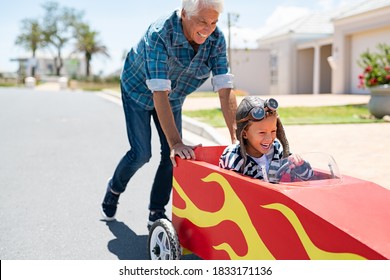 Senior grandfather helping grandson ride on kids toy car. Happy old man pushing car while boy driving on street. Grandparent playing with little boy on gokart.