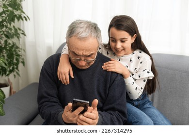 senior grandfather learning to using mobile phone under guidance of pretty young granddaughter sitting on sofa at home - Powered by Shutterstock