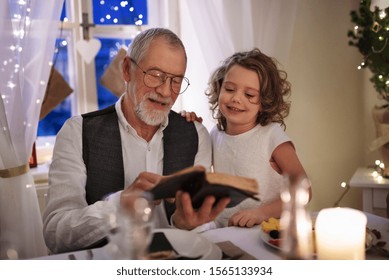 Senior grandfather with small granddaughter indoors at Christmas, reading Bible. - Powered by Shutterstock