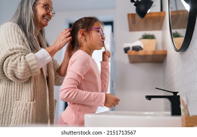 Senior grandmother making a ponytail to her granddaughter indoors in bathroom in the morning.