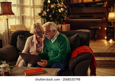 Senior gray hair couple at home celebrating Christmas staying indoors connected to family online on laptop - Powered by Shutterstock