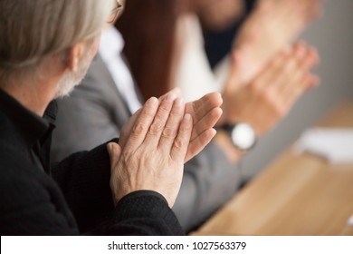 Senior gray-haired businessman clapping hands attending conference, aged training participant applauding at group meeting, old man expressing appreciation or congratulation, rear view, focus on hands - Powered by Shutterstock