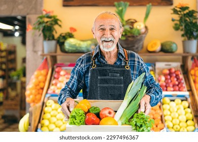 Senior greengrocer working at the market holding a box containing fresh fruits and vegetables - Food retail concept  - Powered by Shutterstock