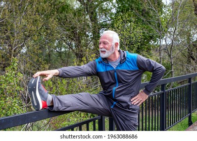 Senior grey bearded man stretching legs outdoors before or after running exercise. Touching his toe tips.