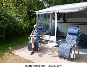 Senior Grey Man Sitting In Front Of The Caravan Using A Mobile Phone For Communication With Other People