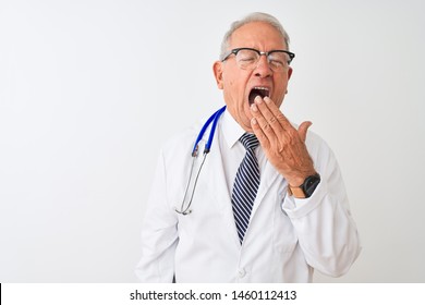 Senior grey-haired doctor man wearing stethoscope standing over isolated white background bored yawning tired covering mouth with hand. Restless and sleepiness.