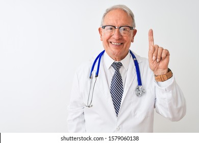 Senior grey-haired doctor man wearing stethoscope standing over isolated white background showing and pointing up with finger number one while smiling confident and happy.