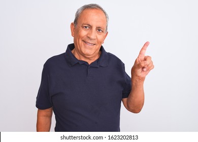 Senior Grey-haired Man Wearing Black Casual Polo Standing Over Isolated White Background With A Big Smile On Face, Pointing With Hand And Finger To The Side Looking At The Camera.