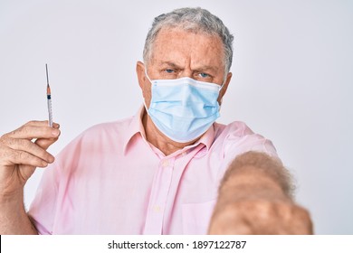 Homme aux cheveux gris, portant un masque médical tenant une seringue pointant du doigt la caméra et vers vous, geste confiant qui a l'air sérieux 