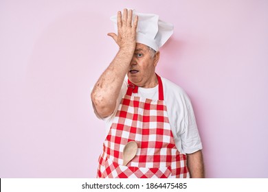 Senior Grey-haired Man Wearing Professional Baker Apron Surprised With Hand On Head For Mistake, Remember Error. Forgot, Bad Memory Concept. 