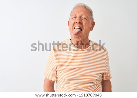 Senior grey-haired man wearing striped t-shirt standing over isolated white background sticking tongue out happy with funny expression. Emotion concept.