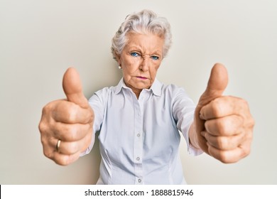 Senior grey-haired woman doing thumbs up positive gesture skeptic and nervous, frowning upset because of problem. negative person. 