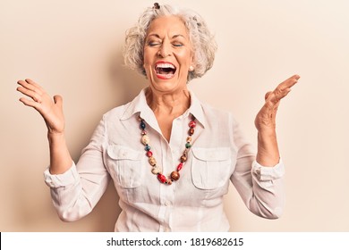 Senior grey-haired woman wearing casual clothes celebrating mad and crazy for success with arms raised and closed eyes screaming excited. winner concept  - Powered by Shutterstock