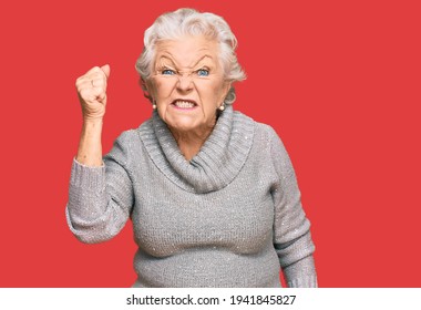 Senior grey-haired woman wearing casual winter sweater angry and mad raising fist frustrated and furious while shouting with anger. rage and aggressive concept.  - Shutterstock ID 1941845827