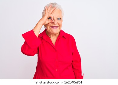 Senior grey-haired woman wearing red casual shirt standing over isolated white background doing ok gesture with hand smiling, eye looking through fingers with happy face.