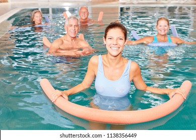 Senior group doing water aerobics in pool with young physiotherapist