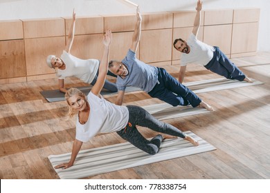 Senior Group Of People With Instructor Exercising On Yoga Mats In Fitness Studio