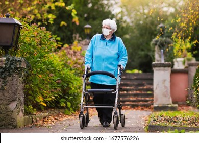 Senior handicapped lady wearing face mask with a walking disability at coronavirus outbreak. Old person in surgical mask pushing walker or wheel chair. Disabled sick patient of nursing home.