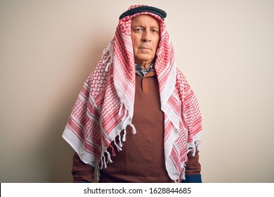 Senior Handsome Arab Man Wearing Keffiyeh Standing Over Isolated White Background With Serious Expression On Face. Simple And Natural Looking At The Camera.