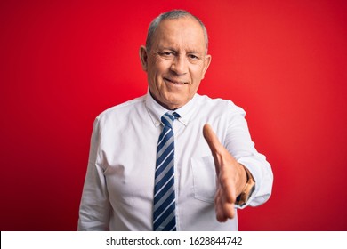 Senior Handsome Businessman Wearing Elegant Tie Standing Over Isolated Red Background Smiling Friendly Offering Handshake As Greeting And Welcoming. Successful Business.