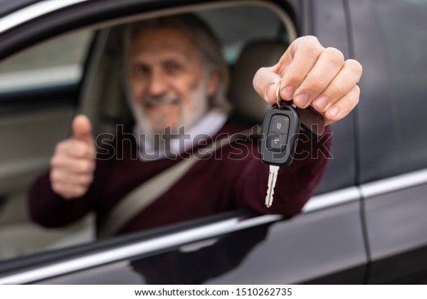 Senior\
handsome driver is showing keys of his new\
car