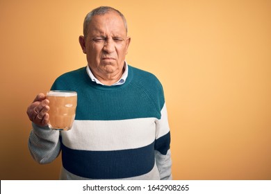 Senior handsome man drinking jar of beer standing over isolated yellow background depressed and worry for distress, crying angry and afraid. Sad expression.