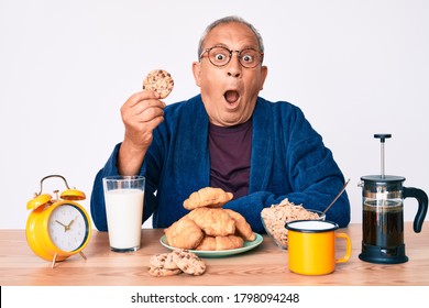 Senior Handsome Man With Gray Hair Sitting On The Table Eating Breakfast In The Morning Scared And Amazed With Open Mouth For Surprise, Disbelief Face 