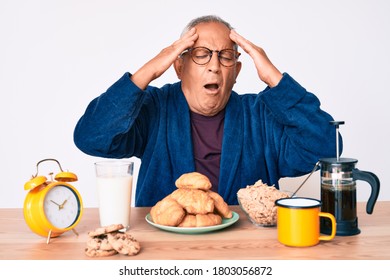 Senior Handsome Man With Gray Hair Sitting On The Table Eating Breakfast In The Morning With Hand On Head, Headache Because Stress. Suffering Migraine. 