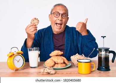 Senior Handsome Man With Gray Hair Sitting On The Table Eating Breakfast In The Morning Pointing Thumb Up To The Side Smiling Happy With Open Mouth 