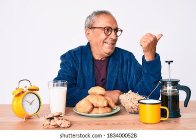 Senior Handsome Man With Gray Hair Sitting On The Table Eating Breakfast In The Morning Pointing Thumb Up To The Side Smiling Happy With Open Mouth 