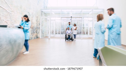 Der gut aussehende Mann im Rollstuhl zieht mithilfe von medizinischem Spezialpersonal im Krankenhaus um 
