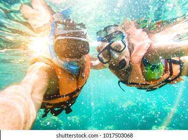 Senior happy couple taking selfie in tropical sea excursion with water camera - Boat trip snorkeling in exotic scenarios - Active retired elderly and fun concept on scuba diving - Warm vivid filter - Shutterstock ID 1017503068