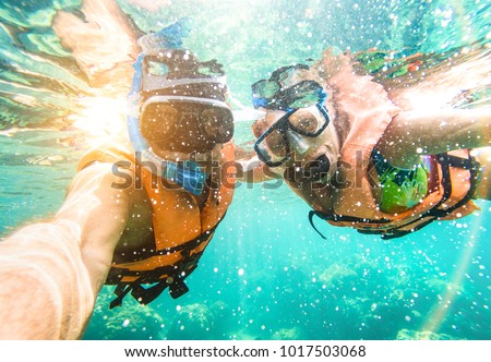 Senior happy couple taking selfie in tropical sea excursion with water camera - Boat trip snorkeling in exotic scenarios - Active retired elderly and fun concept on scuba diving - Warm vivid filter