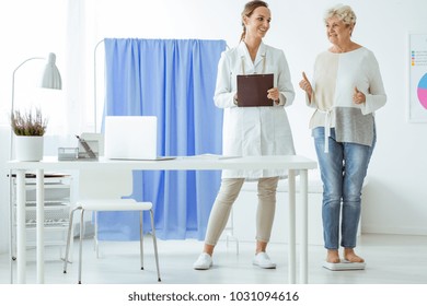 Senior Happy Woman Standing On Scales And Checking Diet Progress During Dietician Consultation