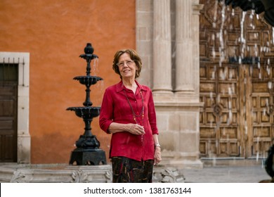 Senior Happy Woman Walking Around A Big Antique House. Mexico