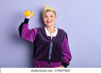 Senior Happy Woman With Yellow Dyed Hair Working Out With Dumbbells At Gum, Close Up Portrait, Isolated Violet Background, Studio Shot, Sport Activity. Lifestyle , Hobby