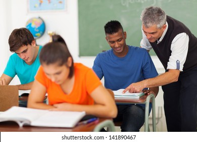 Senior High School Teacher Helping Student In Classroom