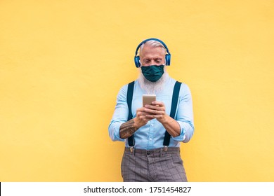 Senior hipster man using phone while listening playlist music on mobile app - Mature guy wearing face protective mask while watching video on smartphone - Coronavirus lifestyle and fashion concept - Powered by Shutterstock